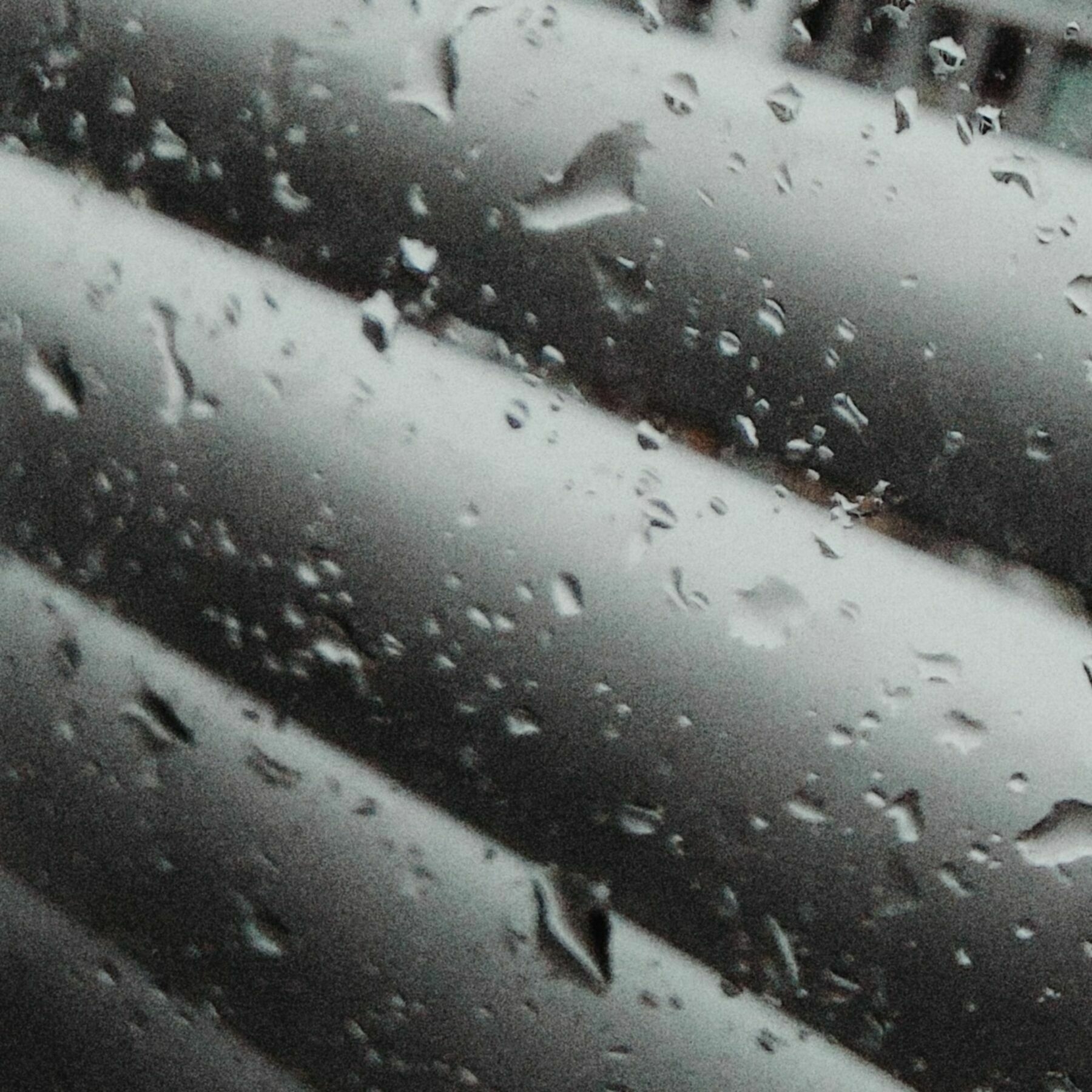 Regentropfen auf Fensterscheiben und Jalousien. Körnig, verwackelt.